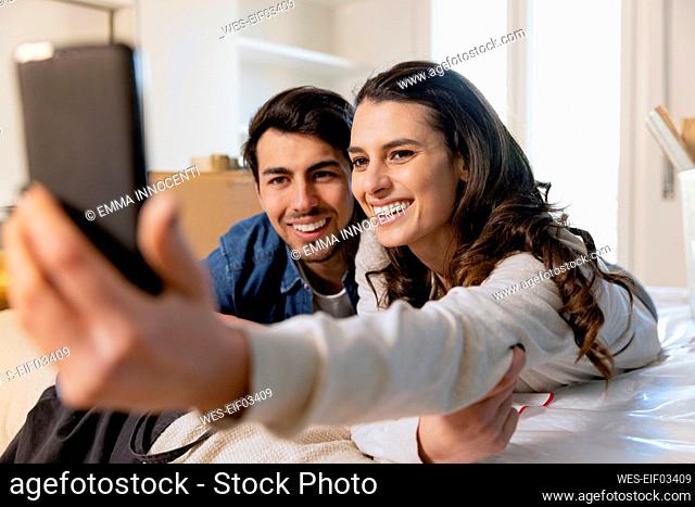 Smiling couple taking selfie on smart phone in bedroom at new home