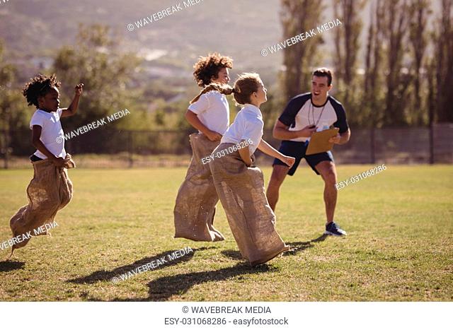 Coach cheering schoolgirls during sack race in park