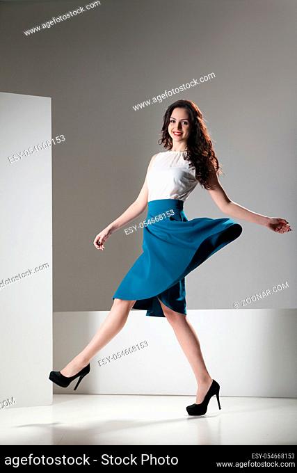 Happy beautiful woman in dark blue skirt and white top walking joyfully and cheerfully smiling. Isolated over grey and white background