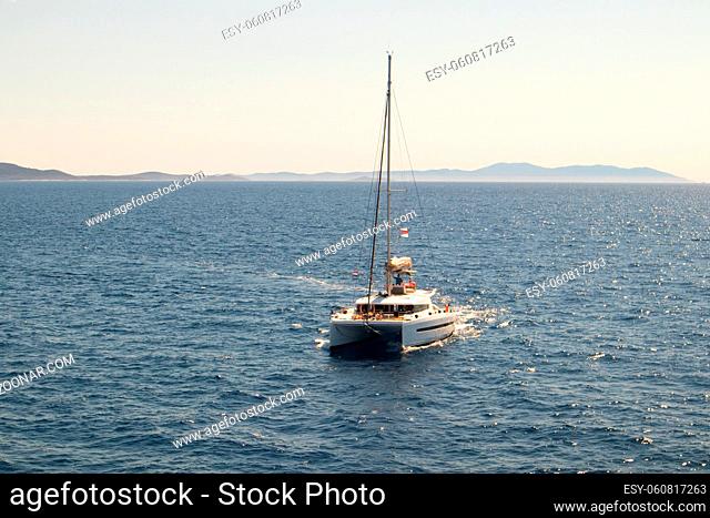 Double-decked catamaran, a yacht with lowered sails, looking towards the horizon. The azure ocean on a sunny day off the coast of Croatia
