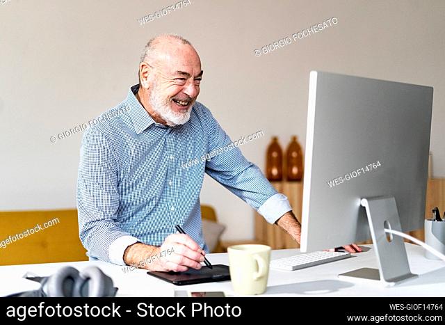 Cheerful freelancer using graphic tablet and computer at desk in home office
