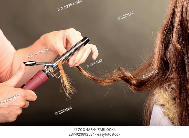 Stylist curling hair for young woman