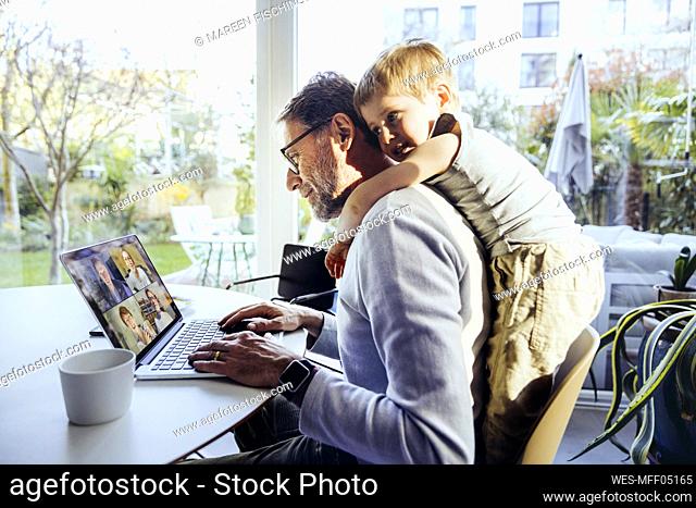 Little boy hugging father from behind, while working from home