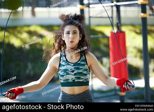 Young slender woman jumping with a rope, boxing workout outdoors at sunny day, close up