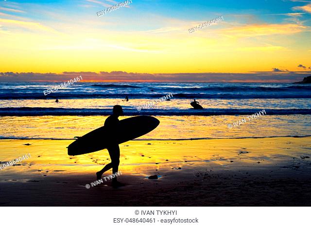 Silhouette of surfer walking by the beach with surfboard at sunset. Bali, Indonesia