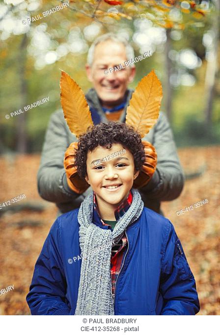 Grandfather holding autumn leaves behind grandson in woods