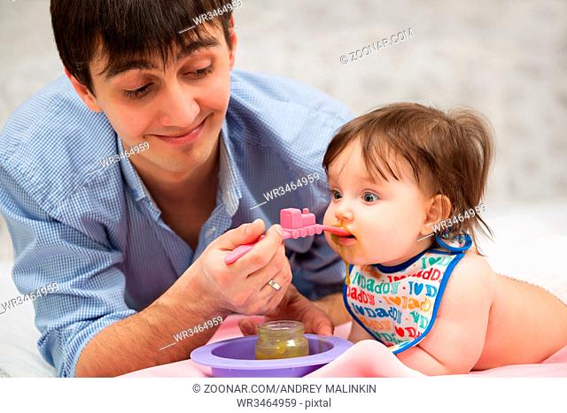Father feeding baby girl on blanket at home