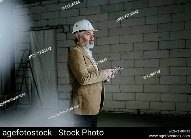 Thoughtful architect standing with tablet PC at construction site