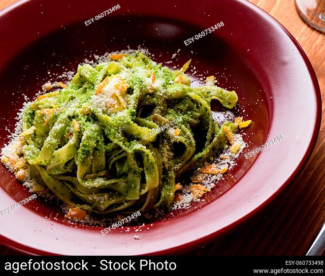 fresh green vegetarian tagliatelle dish in red plate on wooden table