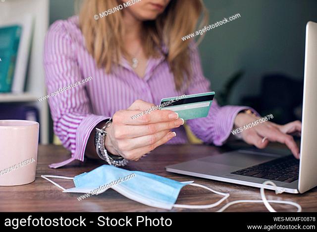 Businesswoman holding credit card making online payment over laptop in office