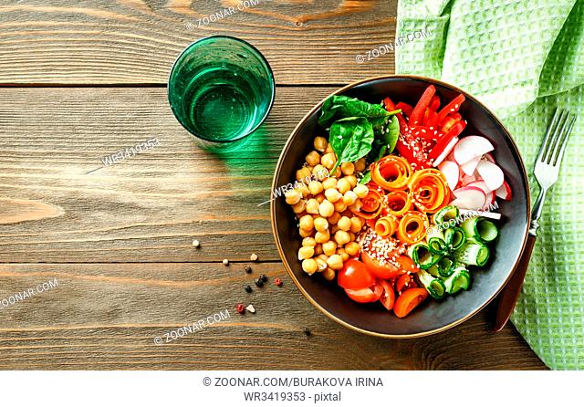 Colorful Buddha Bowl with chickpeas, carrots, tomatoes, cucumbers, radish and peppers on a wooden table. Vegetarian salad. Top view. Space for text