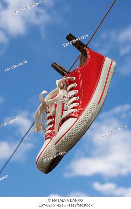 pair of red sneakers hanging on a clothesline on a blue sky background