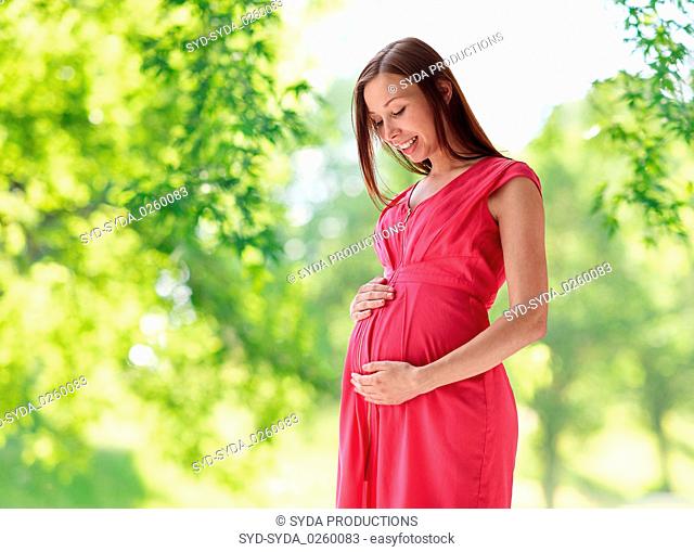 happy pregnant woman touching her belly in summer