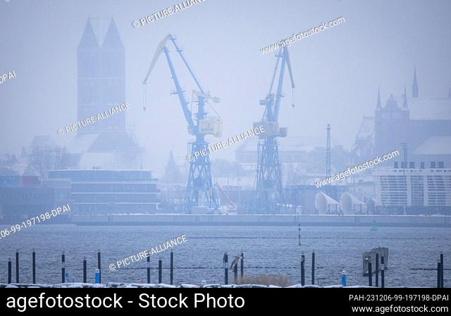 05 December 2023, Mecklenburg-Western Pomerania, Wismar: In heavy snowfall, the old town with the shipyard's cranes is barely visible