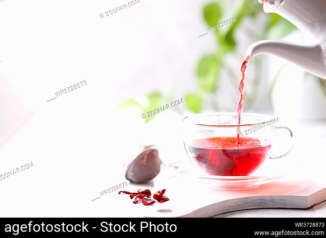 Healthy hibiscus tea in transparent cup on white wooden table in the garden