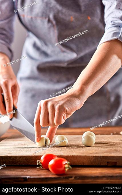 Cook woman in a gray apron cuts boiled quail eggs on a wooden board. Step by Step cooking