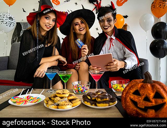 Group of young adult and teenager people celebrating a Halloween party carnival Festival in Halloween costumes and making online shopping with tablet and credit...