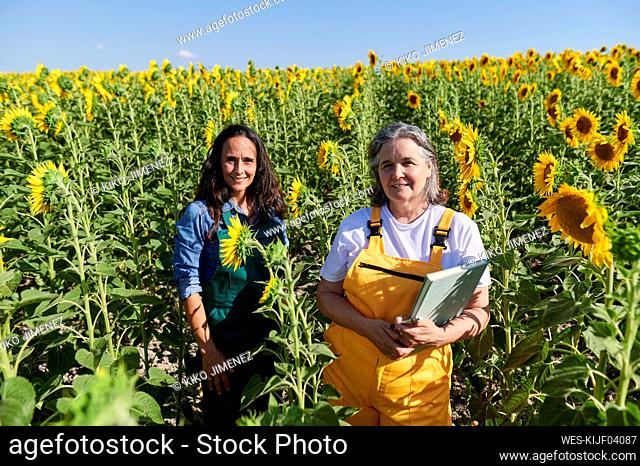 Female farmers standing amidst sunflowers on field during sunny day