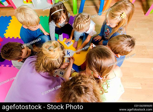 Group of kindergarten kids sitting closely on a floor together with teacher, providing group work. Children learning to cooperate while solving tasks