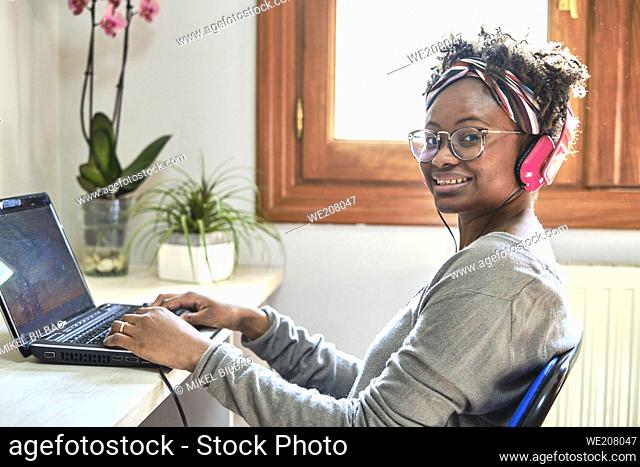 Young black woman with afro hairstyle and a computer and listening music with headphones indoor in a house. Lifestyle concept
