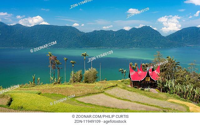 A red tin roofed building in the local Indonesian Batak architecture style sits on a hill over looking the huge crater lake Lake Maninjau, Sumatra, Indonesia