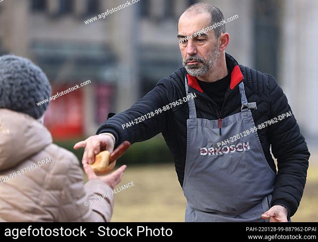 28 January 2022, North Rhine-Westphalia, Duesseldorf: The well-known chef Volker Drkosch (r) hands a roll with a venison sausage to a needy woman