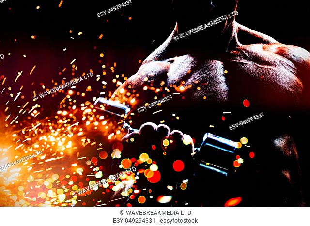 Concentrated bodybuilder lifting dumbbell against firework bursting sparkle background