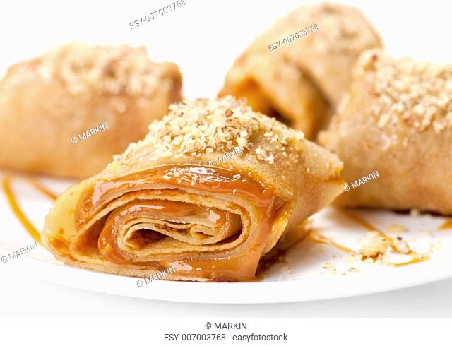 Rolled pancakes with caramel mousse and nuts. On white