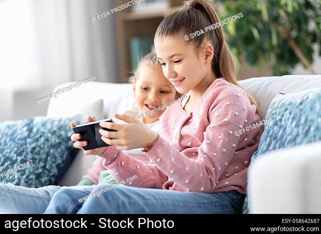 happy little girls or sisters with phone at home