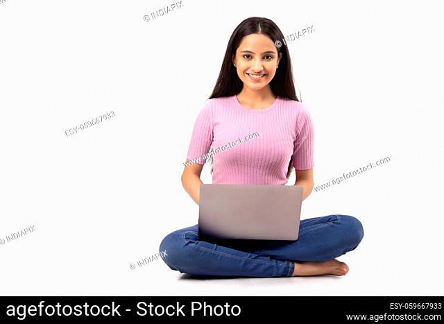 A TEENAGER LOOKING AT CAMERA WHILE SITTING WITH LAPTOP