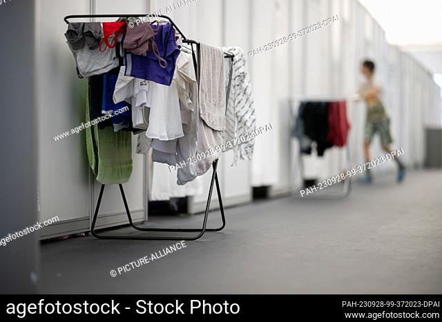 28 September 2023, Berlin: Laundry racks stand in the emergency accommodation for refugees at the former Tegel airport in the living area between two entrances...