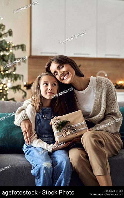 Happy woman with Christmas present embracing daughter in living room