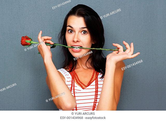 Woman posing with rose between teeth against gray background