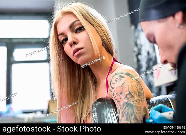 Young sexy blonde in pink top in tatto studio shot with tattoo master drawing colored tiger on girl s forearm
