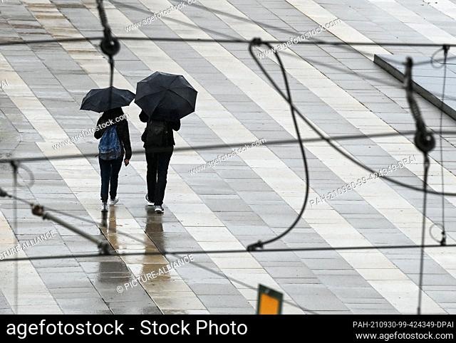 29 September 2021, Brandenburg, Potsdam: Two passers-by with umbrellas walk along the footpath next to Breite Straße under the tram overhead line
