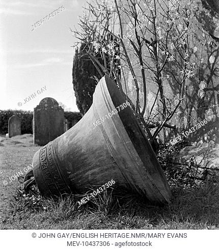 A church bell lying on its side in the churchyard of St Osmond's Church in Melbury Osmond, Dorset