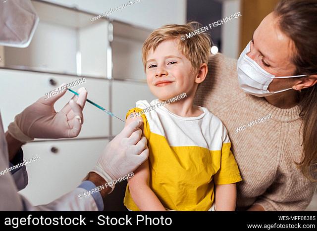 Smiling boy getting vaccine injection by doctor in center