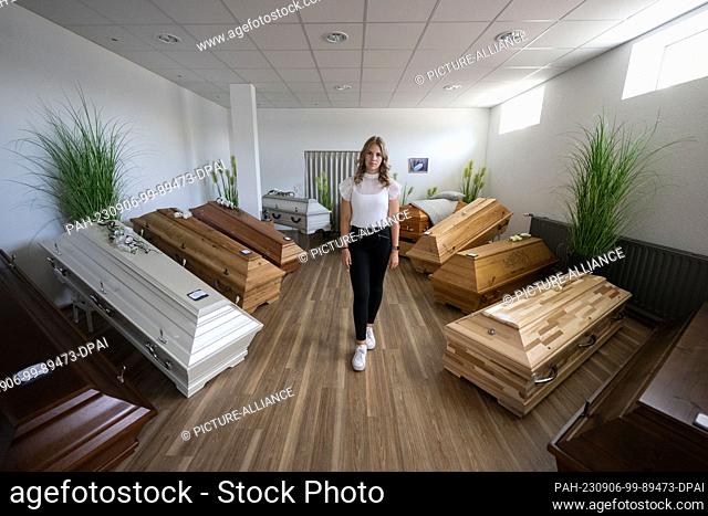 PRODUCTION - 16 August 2023, Baden-Württemberg, Geislingen an der Steige: Mortician Emily Maichle stands in front of coffins in a room at the family-owned...
