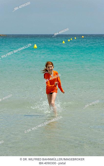 Girl running through the turquoise waters of the Bay of Rondinara, southeast coast, Corsica, France
