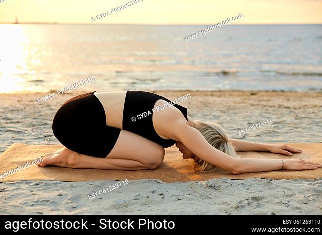woman doing yoga child pose on beach