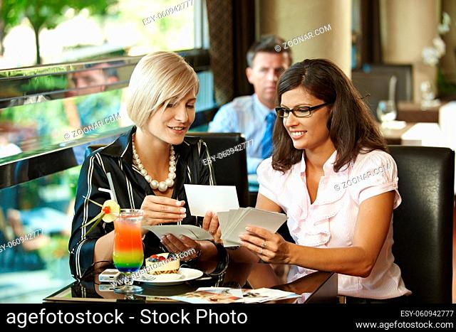 Young women sitting in cafe having sweets, showing photos, smiling