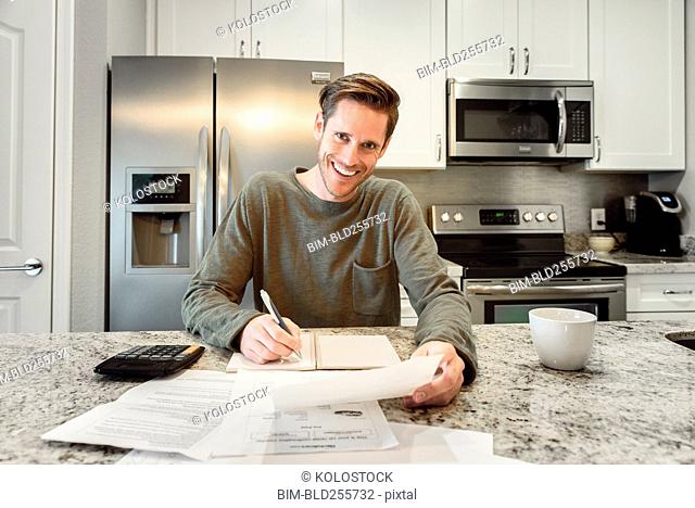 Smiling Caucasian man writing notes and reading paperwork