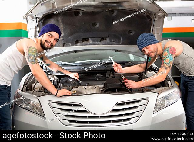 Handsome mechanics working in auto repair shop and solving problems with engine or motor while looking at camera