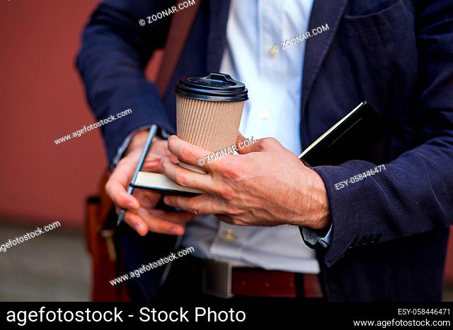 Notepad And Cup Of Coffee Closeup Shot. The Male Writes Information In His Notebook On A Sunny Day. Business Concept Photo