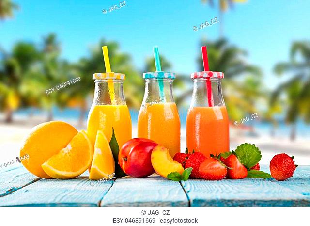 Fresh glasses of juice with fruit mix placed on the beach on wooden planks. Concept of healthy drinks, antioxidants and summer cocktails