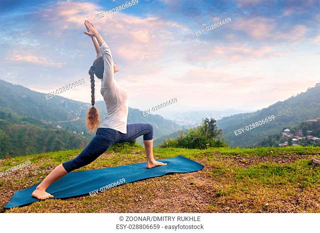 Woman doing yoga asana Virabhadrasana 1 - Warrior pose outdoors