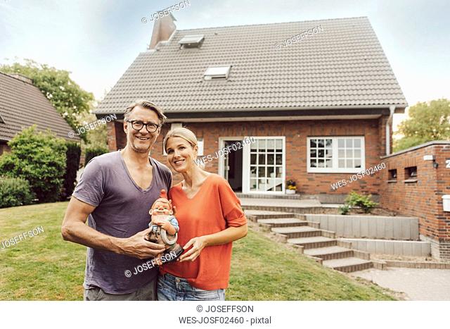Portrait of smiling mature couple standing in front of their home holding garden gnome