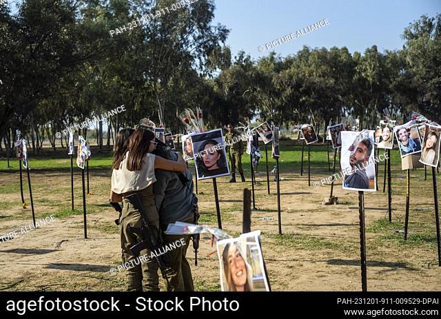 01 December 2023, Israel, Re'im: Israeli soldiers mourn next to the images of the killed Israelis at the site of the Re'im music festival massacre