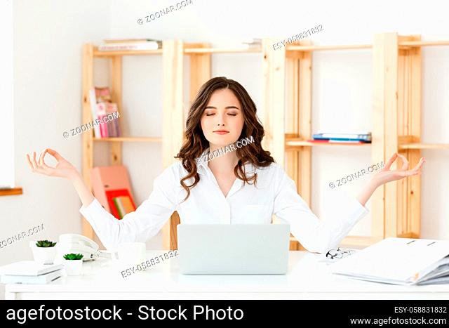 Business and Health Concept: Portrait young woman near the laptop, practicing meditation at the office desk, in front of laptop, online yoga classes
