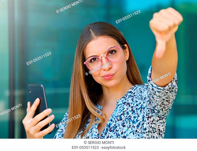 Upset young business woman gives thumb down after watched her new smart phone app